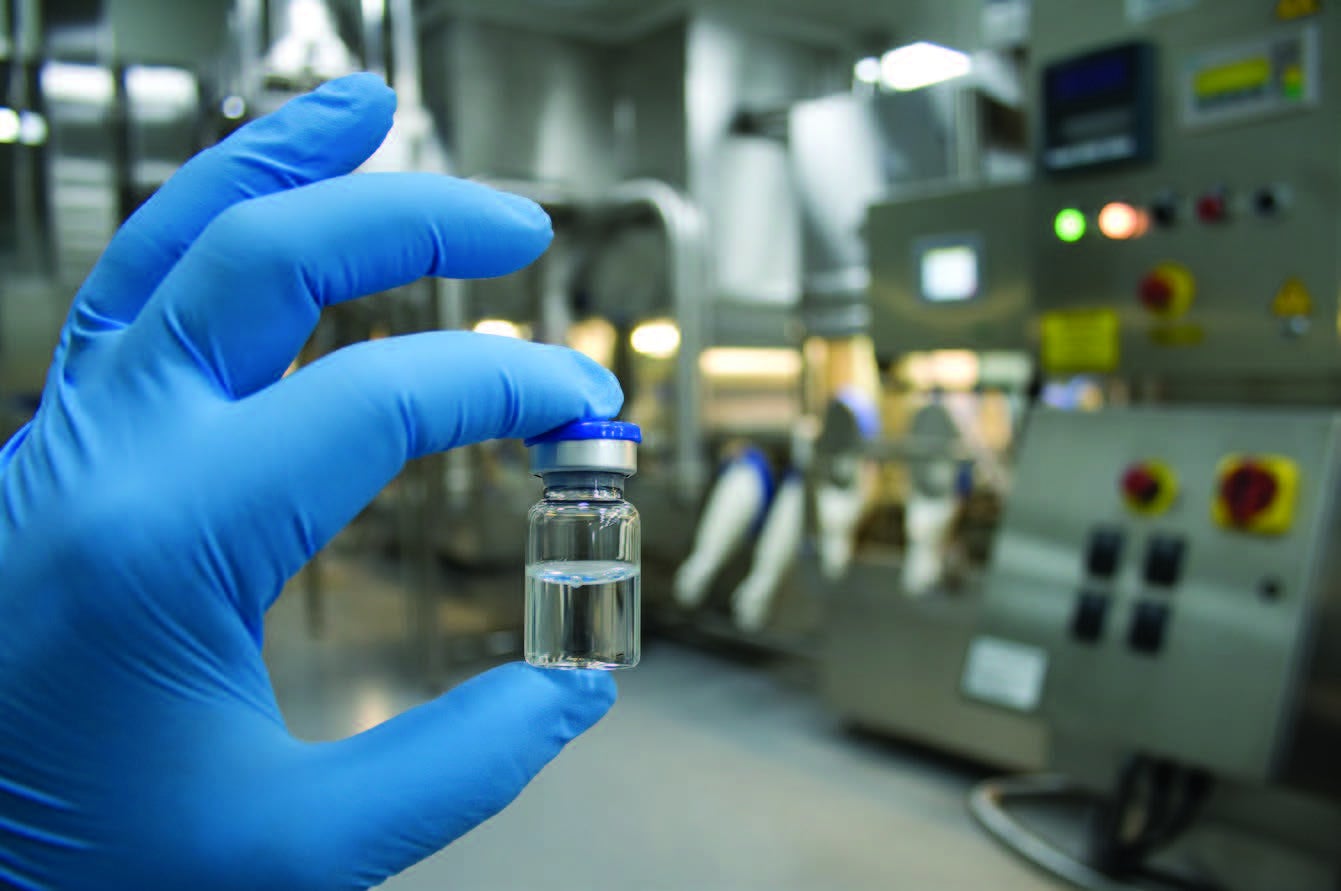 Gloved hand holding a small vial of clear solution