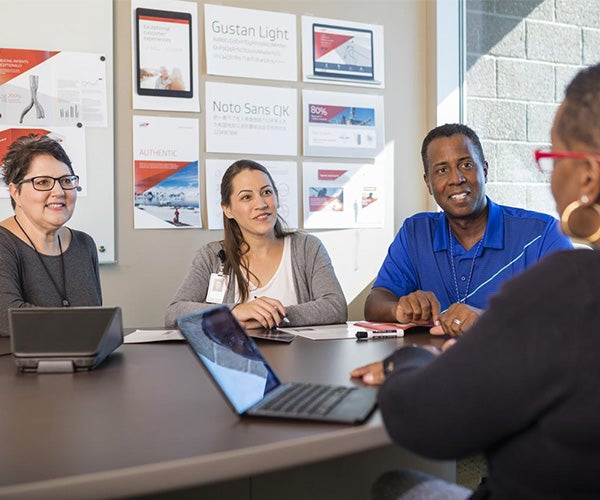 Associates sitting at a table with their computers during a meeting.