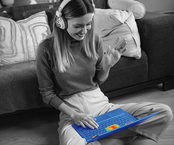 A monochrome photo of a woman using a laptop. Thermal imaging highlights that there are no hotspots on the phone, thanks to GORE® Thermal Insulation.