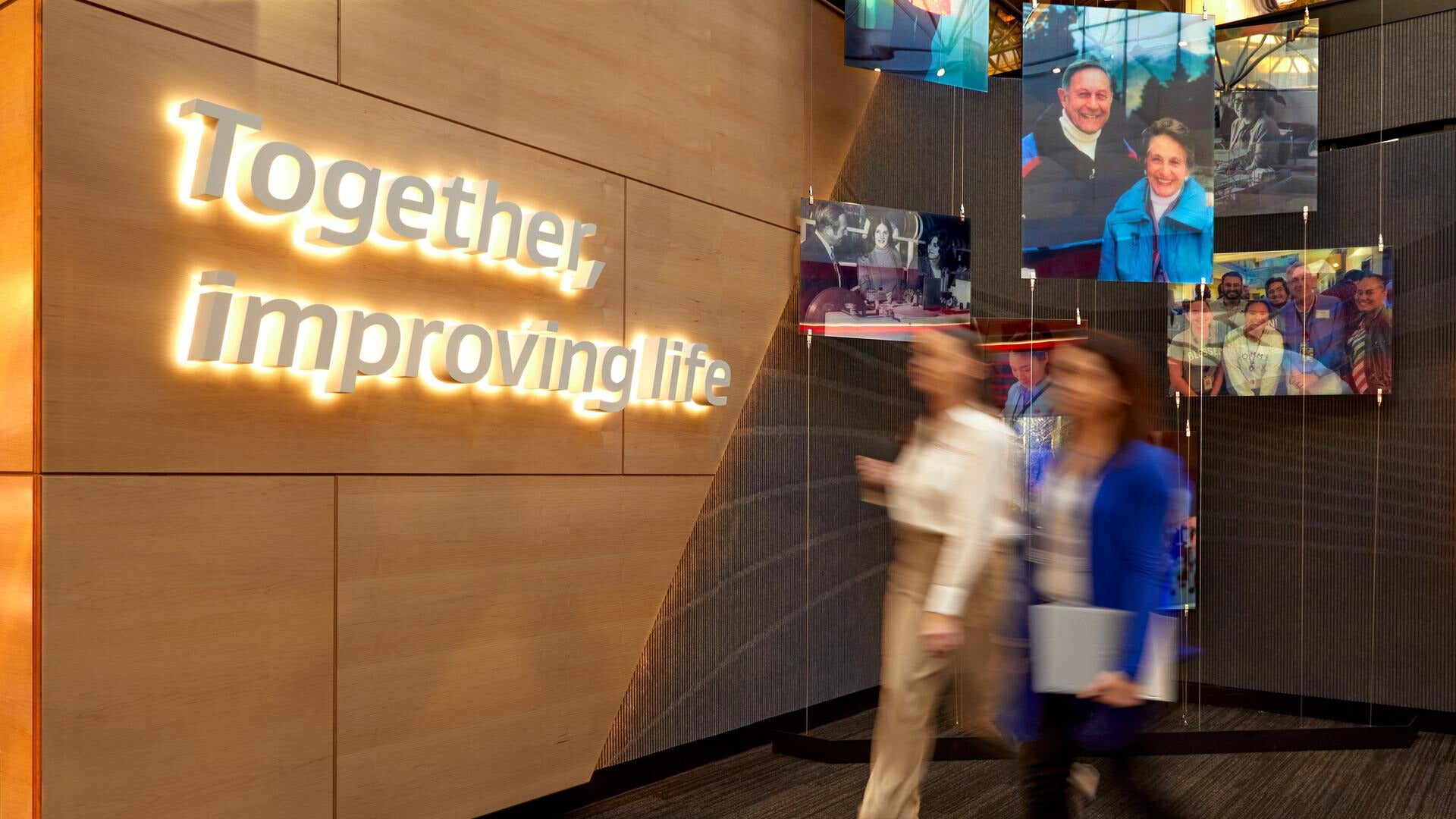 Blurry associates walking through the office with Together, improving life brand promise on the wall