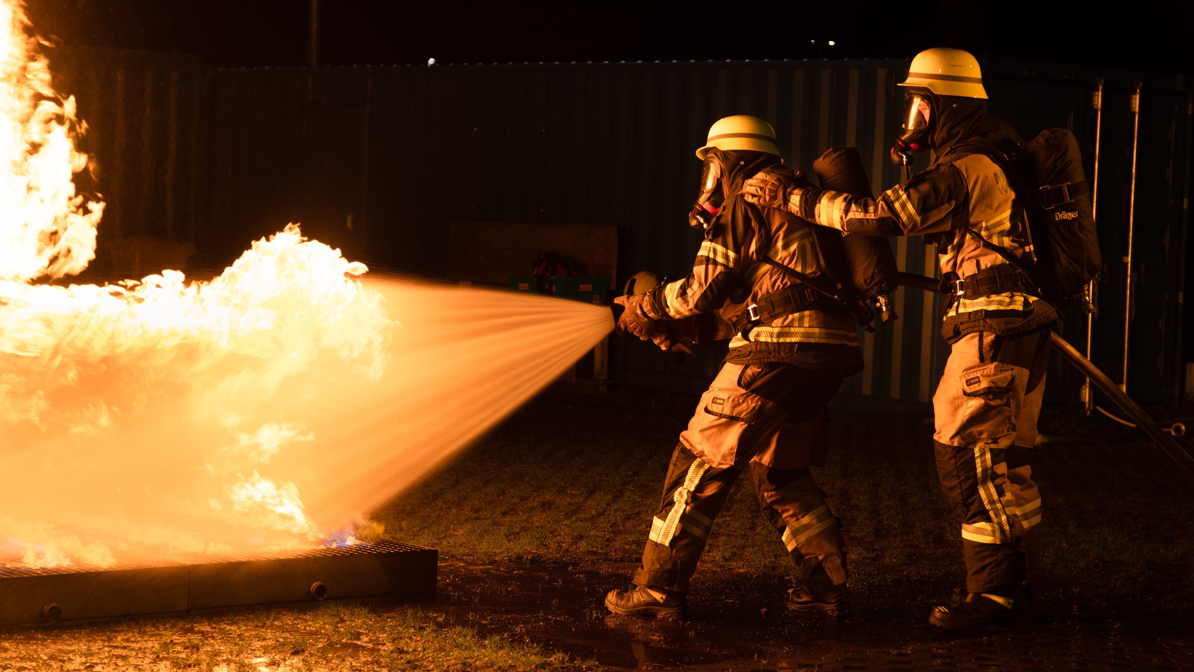 firefighters spraying hose on open flame in darkness