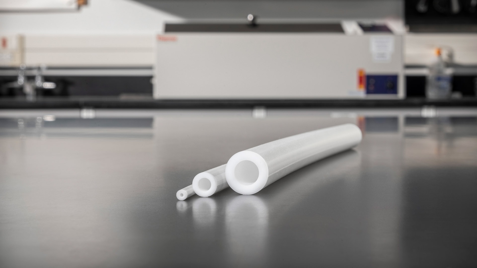 Three white transfer pump tubing sizes displayed on a lab bench with equipment in the background