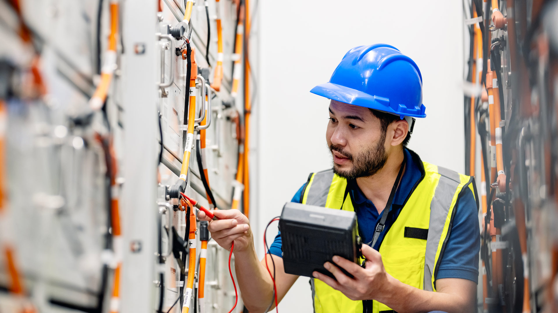 A technician wearing PPE perfoming tests on electrical units using a specialized device