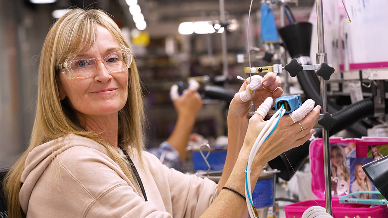 Woman wearing PPE smiling at the camera while operating a specialized machine