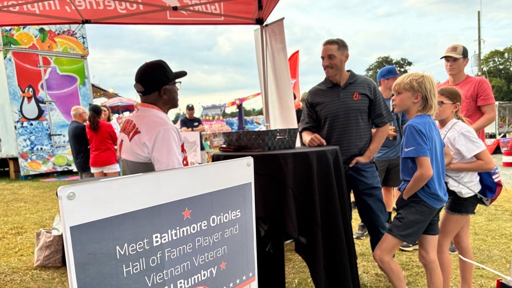 Visitors, including families with children, wait to meet Hall of Fame Baltimore Orioles player and Vietnam veteran Al Bumbry at the Gore booth. A sign reads, “Meet Baltimore Orioles Hall of Fame Player and Vietnam Veteran Al Bumbry.”