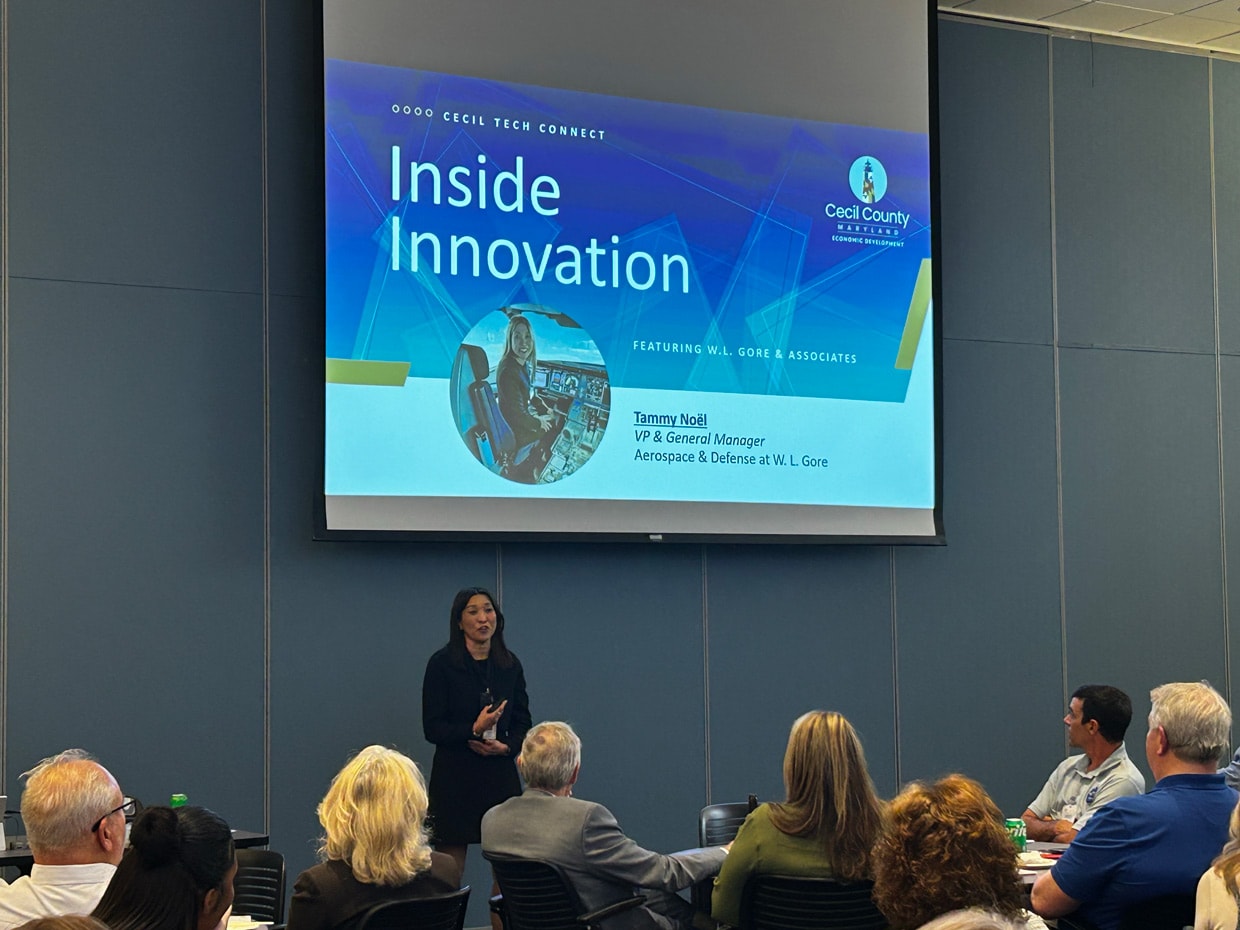 A woman presents to a seated audience during an Inside Innovation event featuring W. L. Gore & Associates, with a projected slide introducing Tammy Noel, VP and General Manager of Aerospace & Defense.