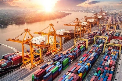 A busy cargo shipping port at sunset, featuring large cranes, hoists and hundreds of shipping containers