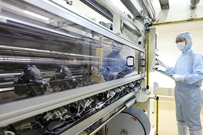 A lab technician in protective clothing inspects a membrane fabrication machine 