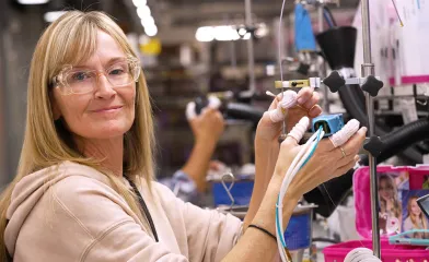 Woman wearing PPE smiling at the camera while operating a specialized machine