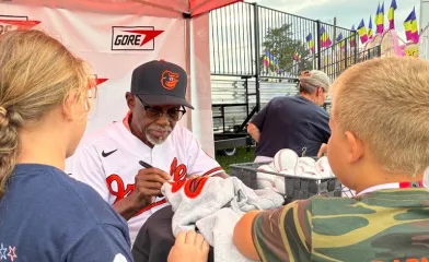 Al Bumbry signs memorabilia for children at the Gore booth during the Cecil County Fair, seated at a table with baskets of baseballs ready for autographs.