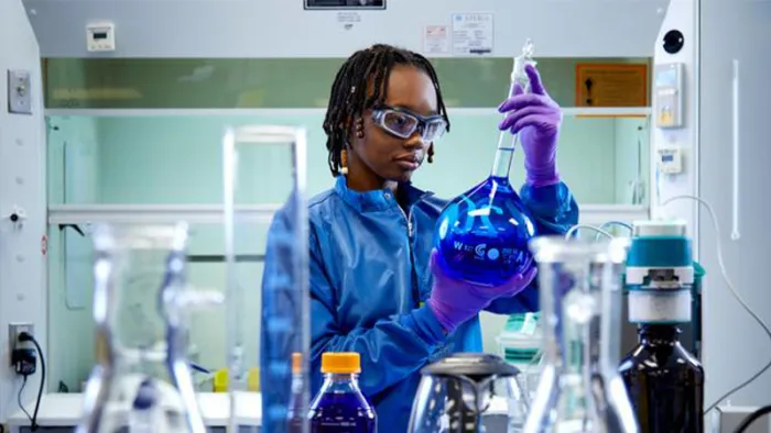 Woman using PPE viewing a large bottle in a lab.