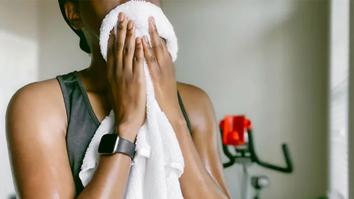 Woman wearing a watch wiping her face with towel at the gym