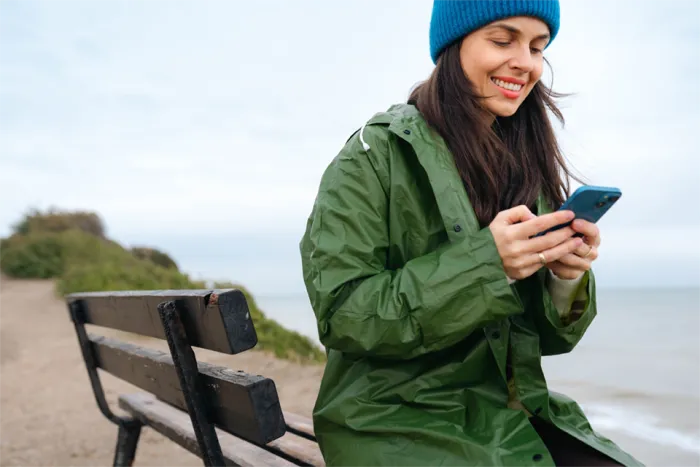Woman sitting on a bench in front of the ocean using her smartphone.