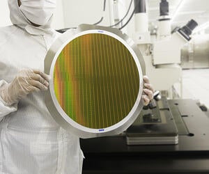 Semiconductor cleanroom technician holding a silicon wafer disc.