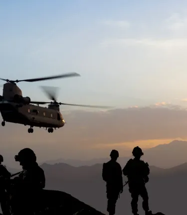 Helicopter and soldiers in front of a sunset.