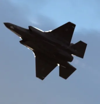 An aircraft flying swiftly under a cloudy sky.