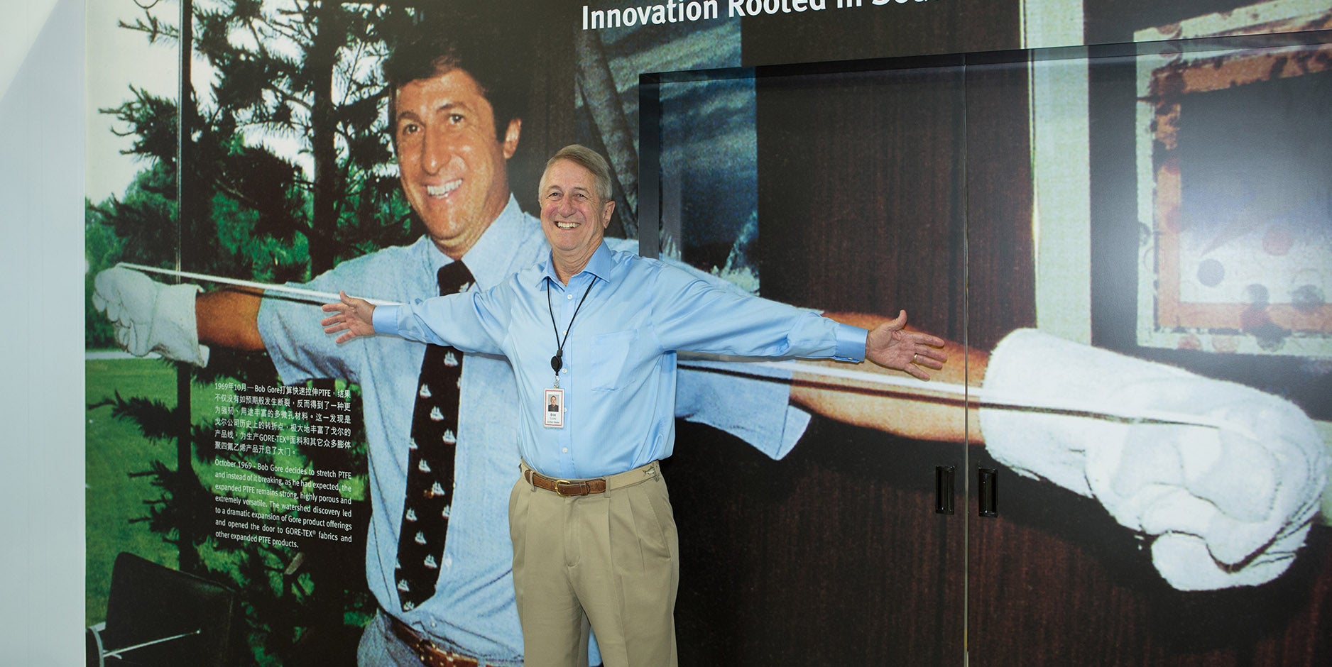 Bob Gore standing in front of a picture of himself stretching PTFE.